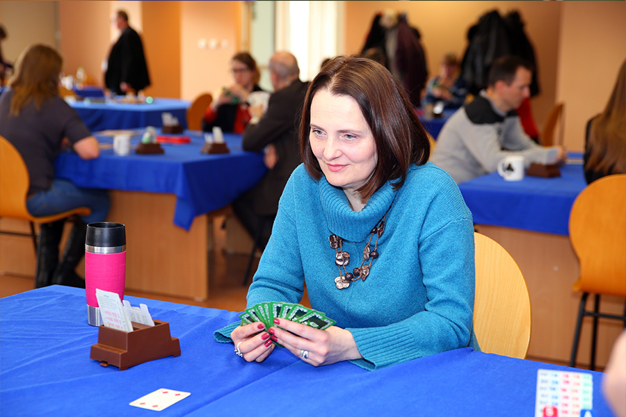 na zdjęciu kobieta przy stoliku z kartami do gry w ręce