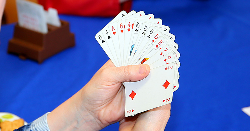 na zdjęciu kobieta przy stoliku z kartami do gry w ręce