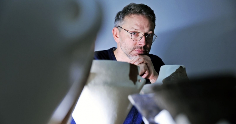 Przed dr. Kamilem Adamczakiem z Katedry Prahistorii w Instytucie Archeologii UMK stoją zrekonstruowane naczynia prehistoryczne