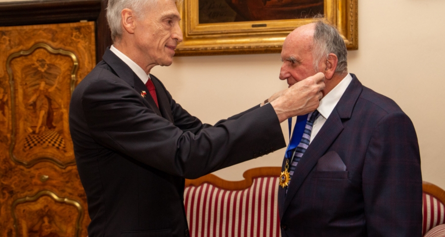 Dwóch mężczyzn, jeden w podeszłym wieku odbierający medal z rąk drugiego. 