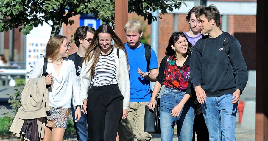Grupa studentów i studentek idzie przez kampus UMK, rozmawiają i uśmiechają się