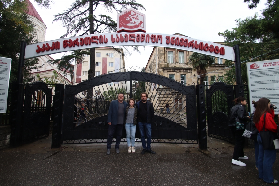 Three people against the background of the entrance gate and university buildings