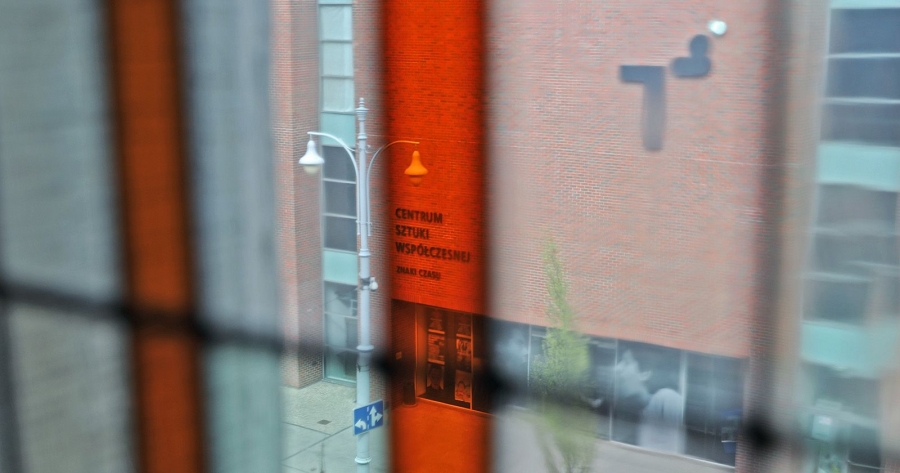 Widok na budynek CSW zza zamkniętego okna z budynku naprzeciwko. Napis na budynku 