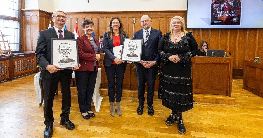 Pięć osób pozujących do oficjalnego zdjęcia z dyplomami i karykaturalnym obrazkiem