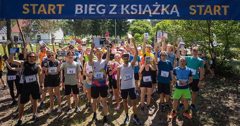 na zdjęciu biegacze z książkami w rękach pod banerem Biegu z książką