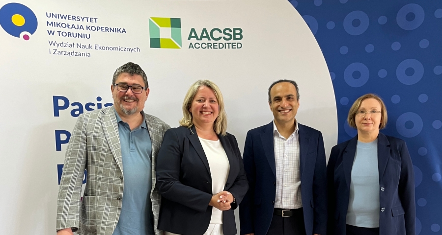 3 nauczycieli akademickich WNEiZ UMK i profesor z Australii stoją na tle logo wydziału i logo AACSB.