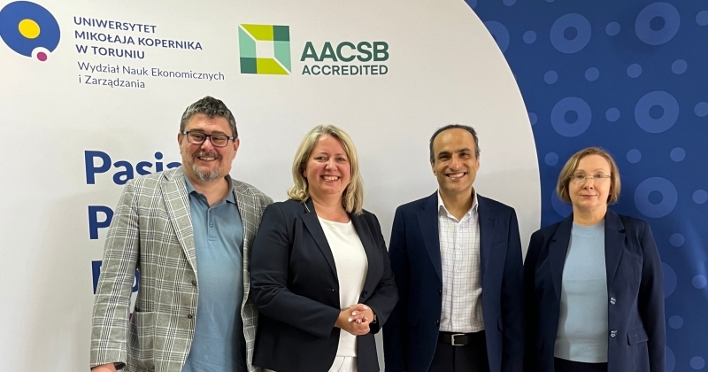 4 professors standing on the background with faculty and aacsb logos.
