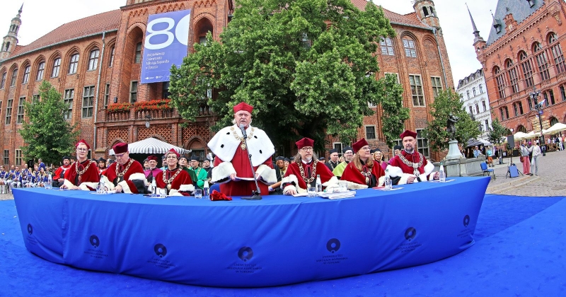 Rector and pro-rectors at a table covered with a blue tablecloth. Old Town Hall in the background