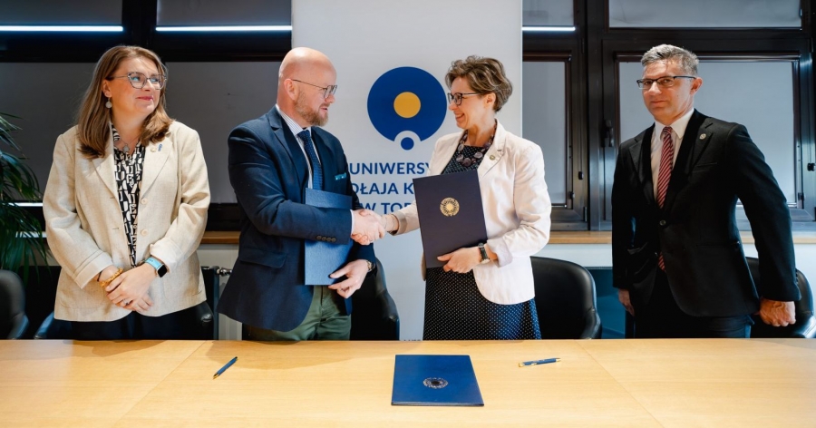 Prorektorka UMK i Rzecznik Finansowy podają sobie ręce na tle roll-upu z logo UMK. Po bokach stoją druga prorektorka i prodziekan Wydziału Prawa