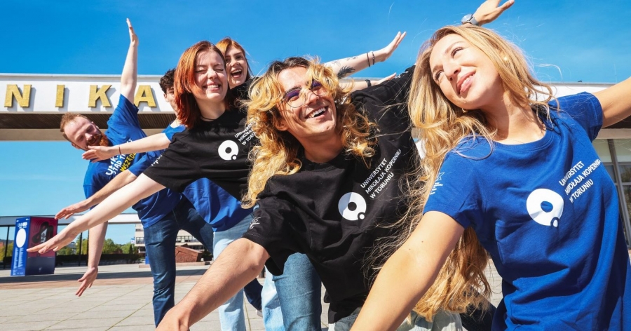 Grupa uśmiechniętych studentów i studentek UMK z rozłożonymi ramionami - jakby szykowali się do lotu