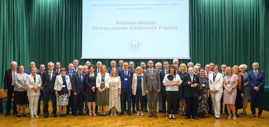 Na scenie, na tle zielonej kurtyny, stoi liczna grupa kobiet i mężczyzn w różnym wieku.