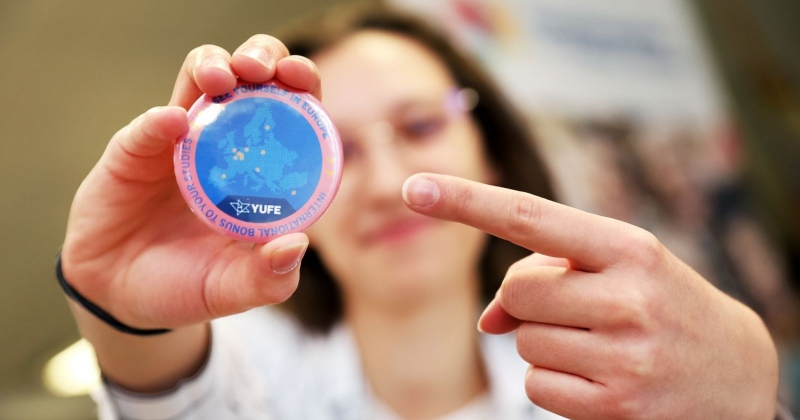 Dziewczyna trzyma w ręku przypinkę YUFE i pokazuje na nią palcem