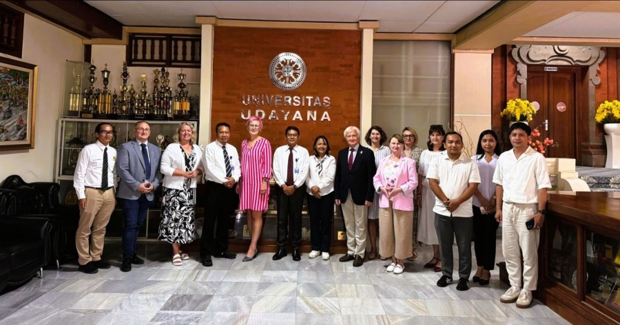 ChatGPT powiedział:  15 people ? a delegation from Nicolaus Copernicus University and representatives of Udayana University ? are standing in a row. In the background, the logo of the Indonesian university is visible