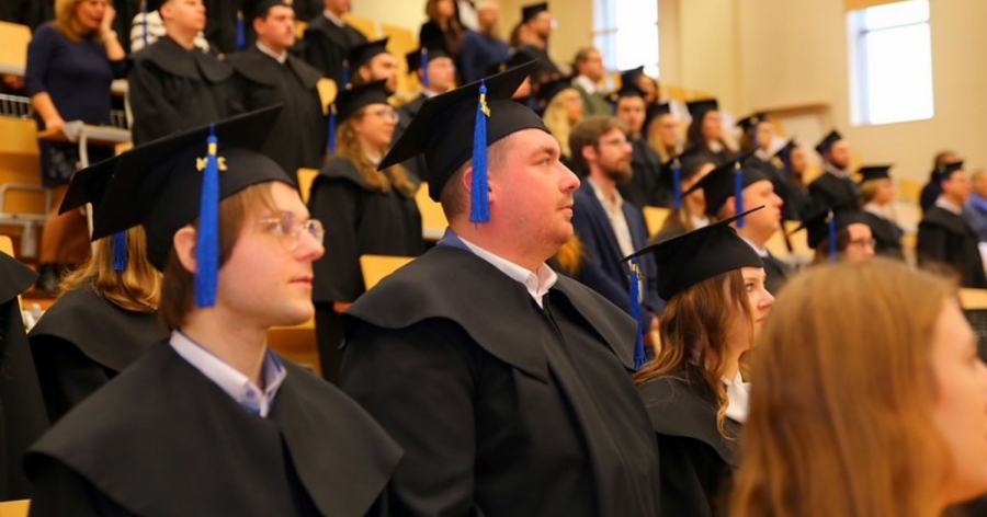 Zdjęcie przedstawia twarze stojących absolwentów w togach i biretach