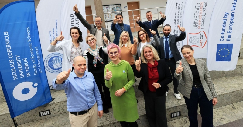 Grupa kilkunastu osób pracujących nad projektem, uśmiechają się, pokazują podniesiony kciuk