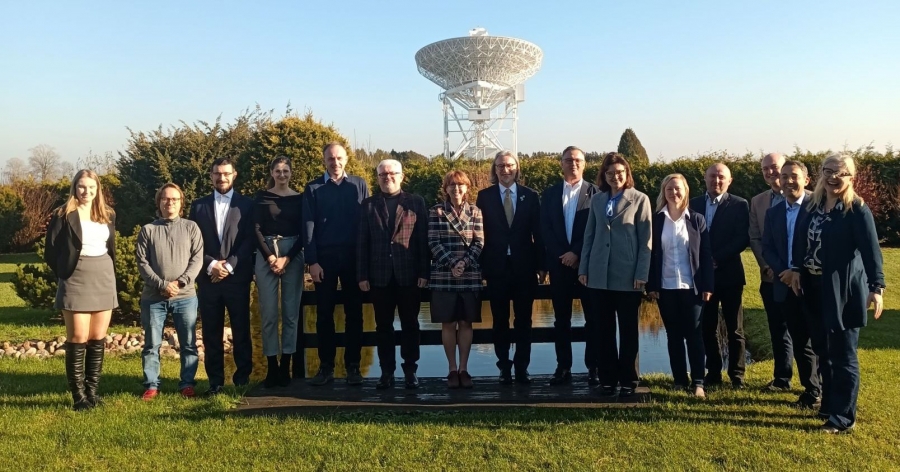 A dozen or so people are standing in line outside, with a radio telescope located at the Nicolaus Copernicus University astronomical observatory in Piwnice visible in the background.