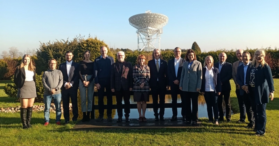 Kilkanaście osób stoi w rzędzie na zewnątrz, w tle widać radioteleskop znajdujący się w obserwatorium astronomicznym UMK w Piwnicach