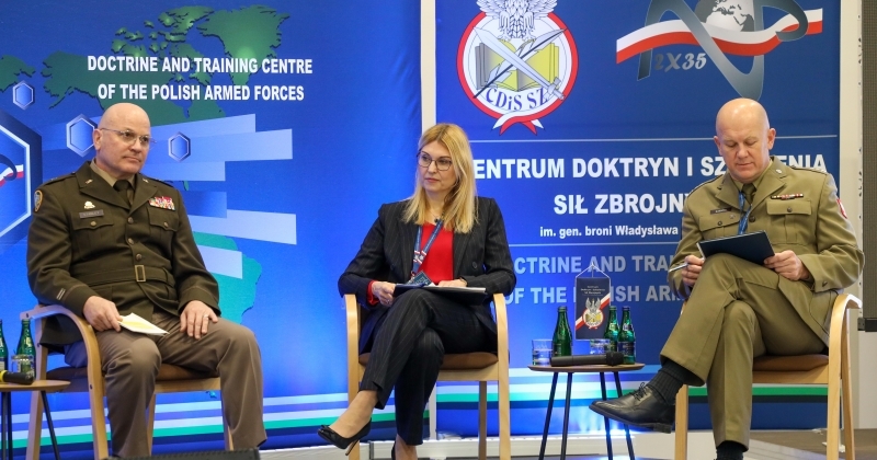 Two men in military uniforms, one women in civil clothing siting on a stage.
