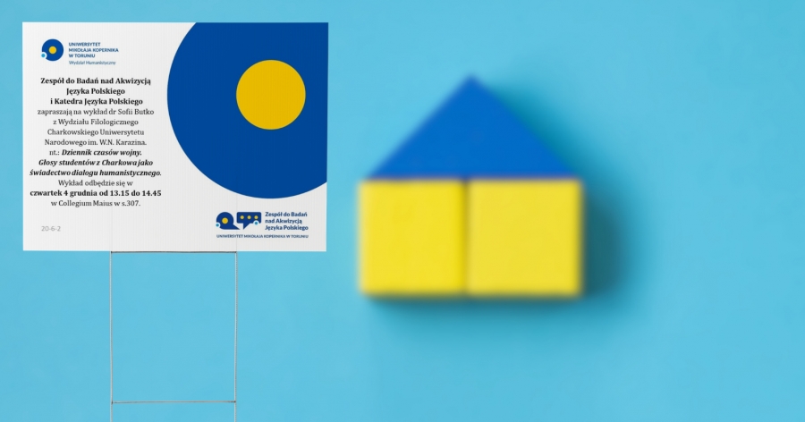 Na pierwszym planie tablica z informacjami o wykładzie dr Sofii Butko. W tle klocki - w kolorach flagii Ukrainy - ułożone w dom.