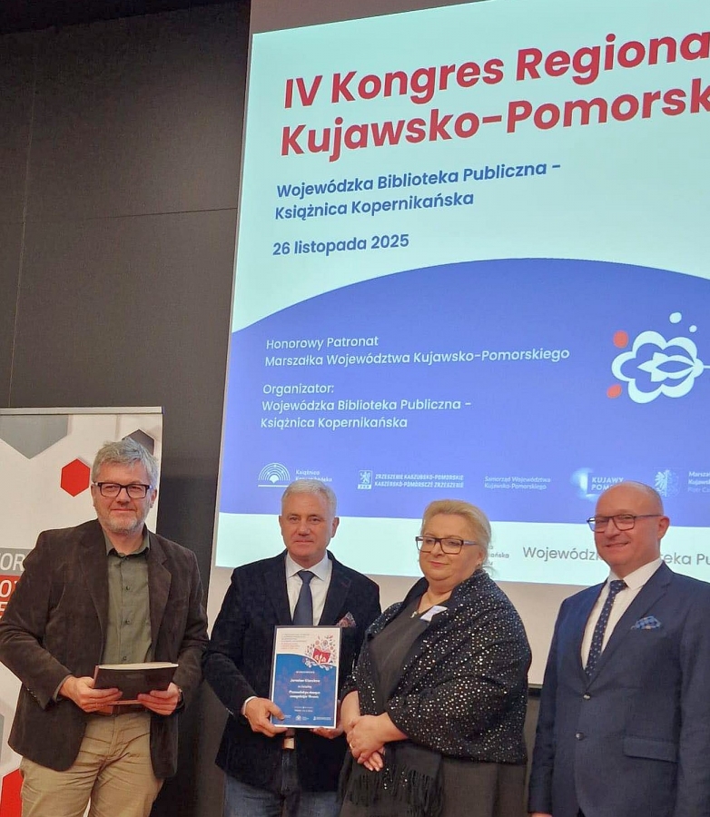 Trzech mężczyzna i jedna kobieta stoją na scenie poniżej obrazu wyświetlanego przez projektor i pozują do zdjęcia.