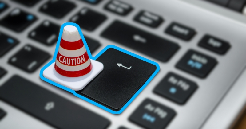 Klawiatura komputera. Na przycisku enter stoi miniaturowy stożek z napisem CAUTION.