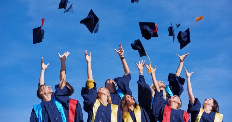 Grupa absolwentek i absolwentów ubrana w togi rzuca do góry biretami