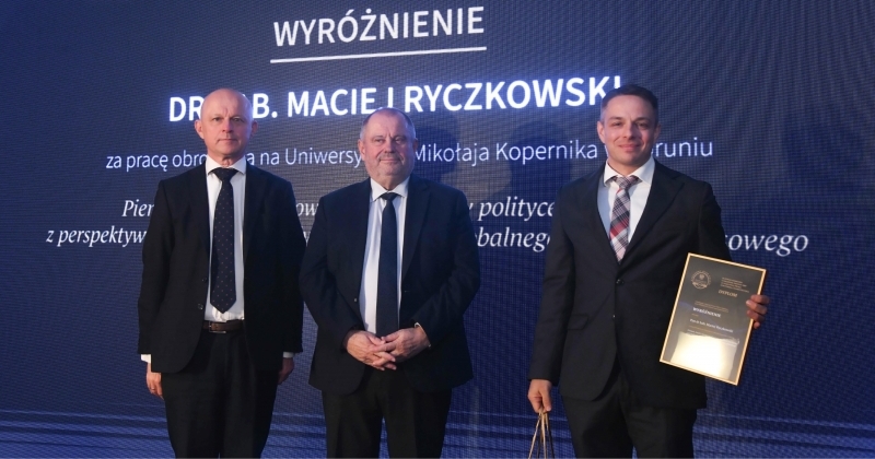 Dwóch mężczyzn oraz dr hab. Maciej Ryczkowski odbieracjący nagrodę na scenie