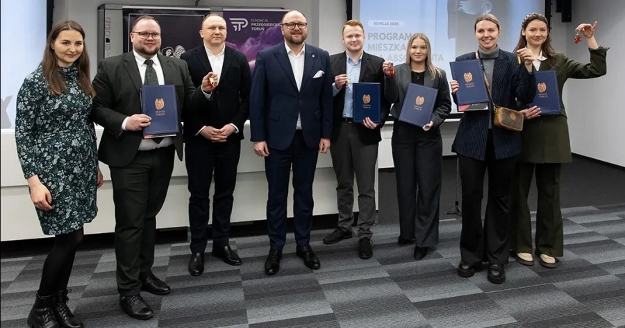 Absolwenci UMK pozują do zdjęcia z teczkami i kluczami do mieszkań