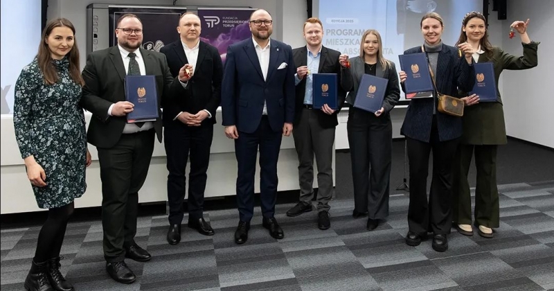 Absolwenci UMK pozują do zdjęcia z teczkami i kluczami do mieszkań