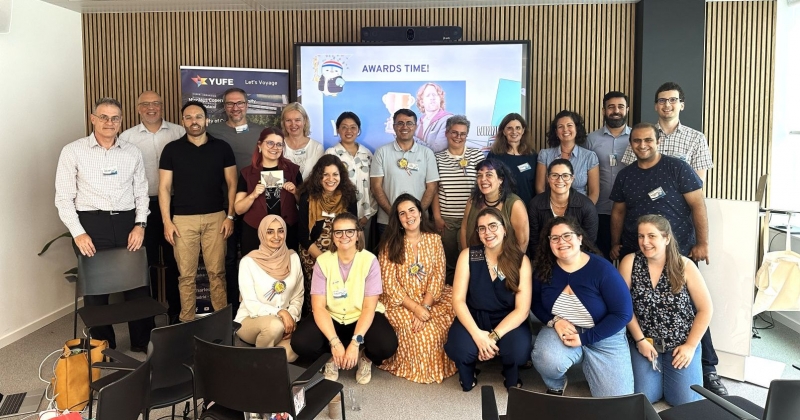 Grupa kilkunastu naukowców i naukowczyń z różnych uczelni YUFE. W tle ekran z napisem AWARDS TIME!