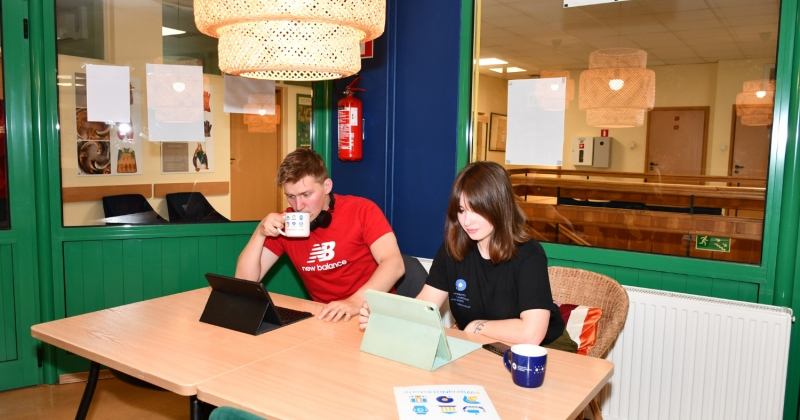 Dwoje studentów siedzących przed komputerami i pijących kawę.