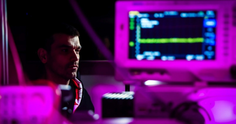 Profesor Piotr Wcisło siedzi w laboratorium w różowej poświacie.