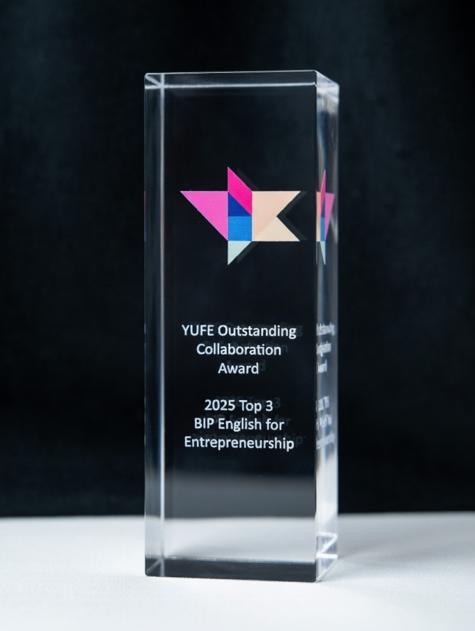 Zdjęcie wykonane w przestrzeni parku. Na pierwszym planie stand z dużym plakatem konferencyjnym. Obok plakatu stoją trzy uśmiechnięte osoby, uczestnicy projektu  ?English for Entrepreneurship?.