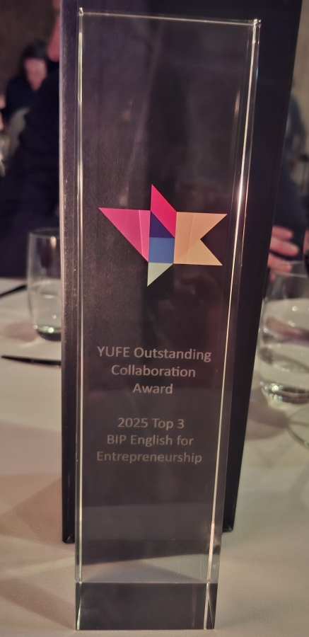 This photo was taken in a park. In the foreground is a stand with a large conference poster. Next to the poster stand three smiling people, participants of the 