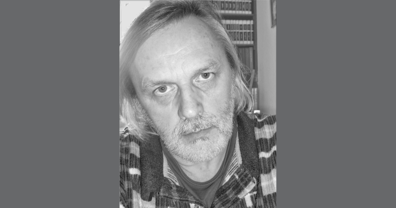 Zdjęcie w szarościach przedstawiającego twarz starszego mężczyzny z krótkim zarostem i dłuższymi włosami