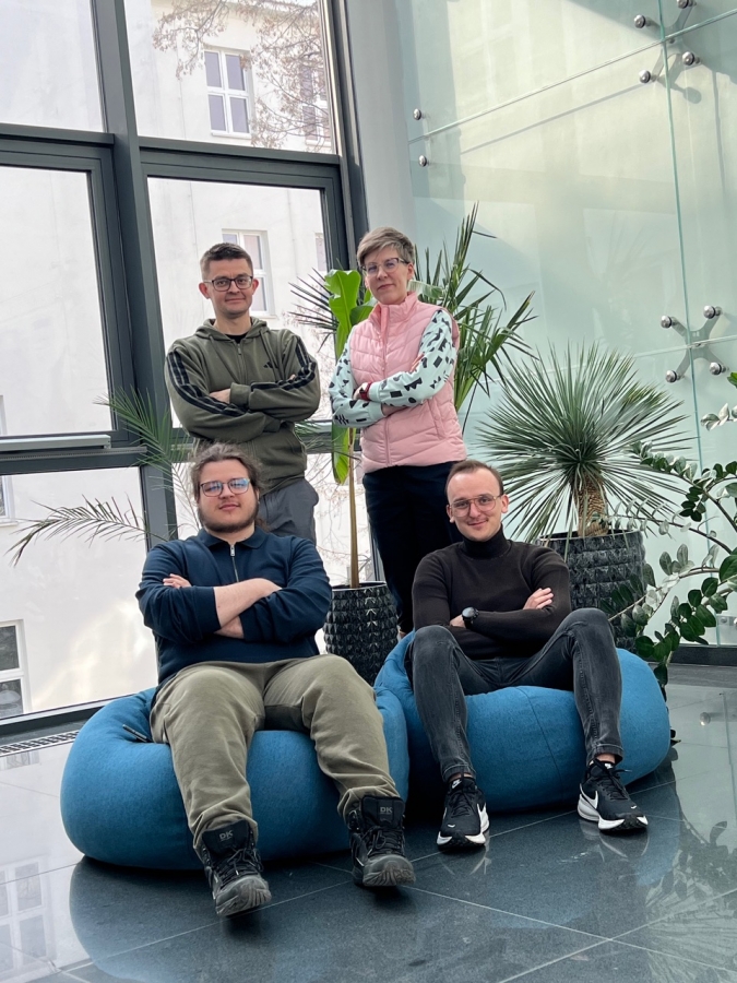 Dwie siedzące osoby na pufach, z tyłu stojące osoby, grafika zawiera też ogłoszenie wyników przyznania stypendiów przez Ministerstwo Nauki 