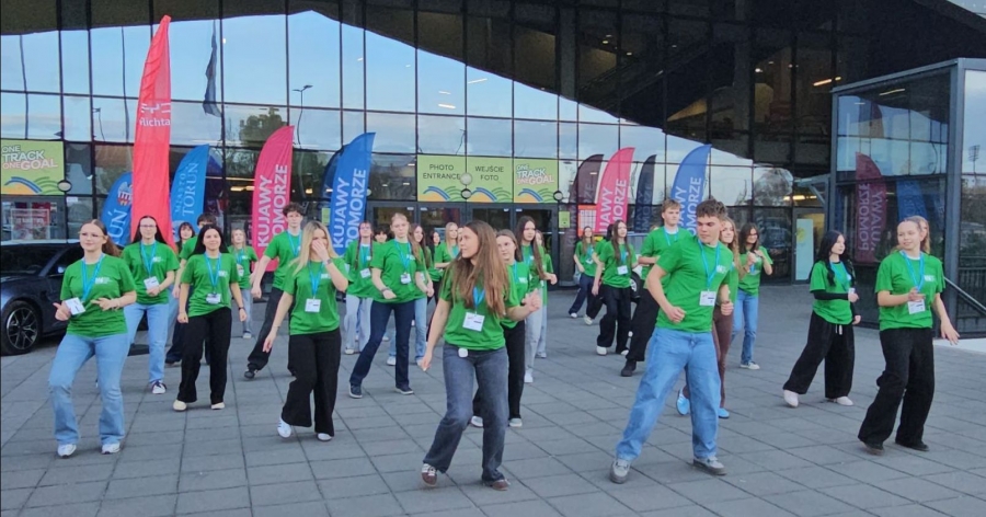 Grupa młodych ludzi w zielonych koszulkach prezentuje układ taneczny