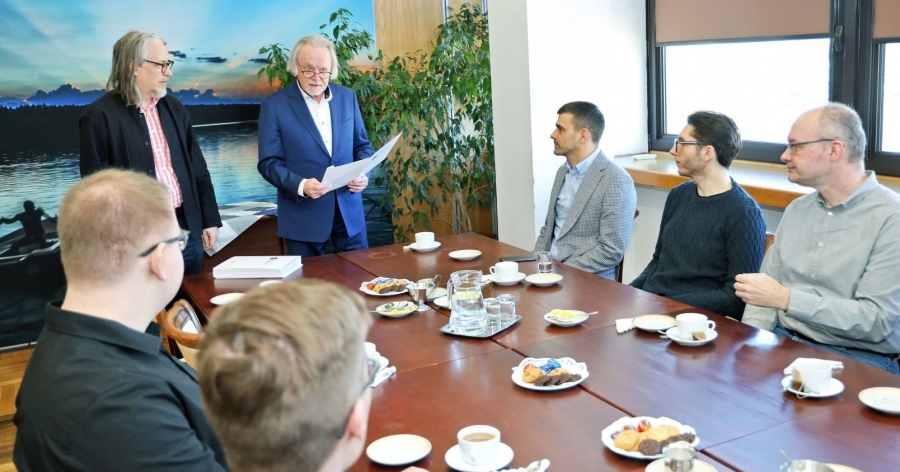 Pięciu mężczyzn siedzi przy stole. Stoją też przy nim dwie osoby: rektor i prorektor uniwersytetu