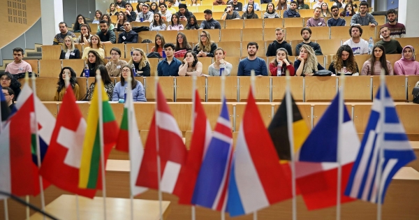 Międzynarodowe flagi, w tle studenci w sali wykładowej