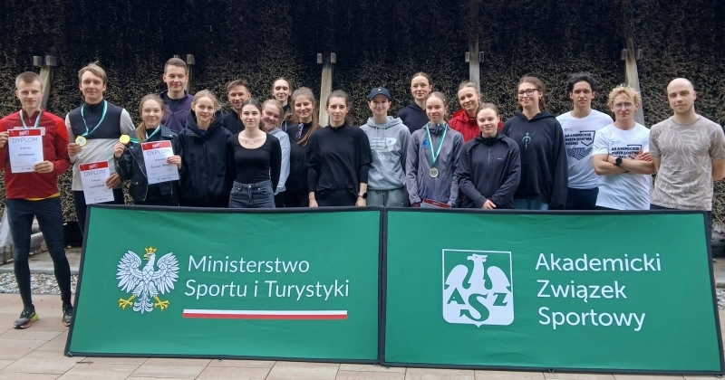 Uczestnicy Akademickich Mistrzostw Pomorza i Kujaw w biegach przełajowych pozują do wspólnego zdjęcia pamiątkowego przed tężnią solankową, prezentując zdobyte medale i dyplomy obok banerów Ministerstwa Sportu i Turystyki oraz Akademickiego Związku Sportowego.
