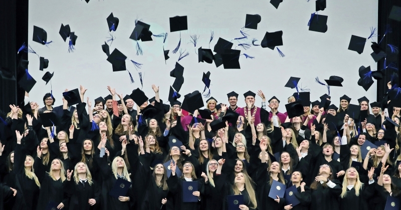 na zdjęciu absolwenci w togach podrzucający birety w górę